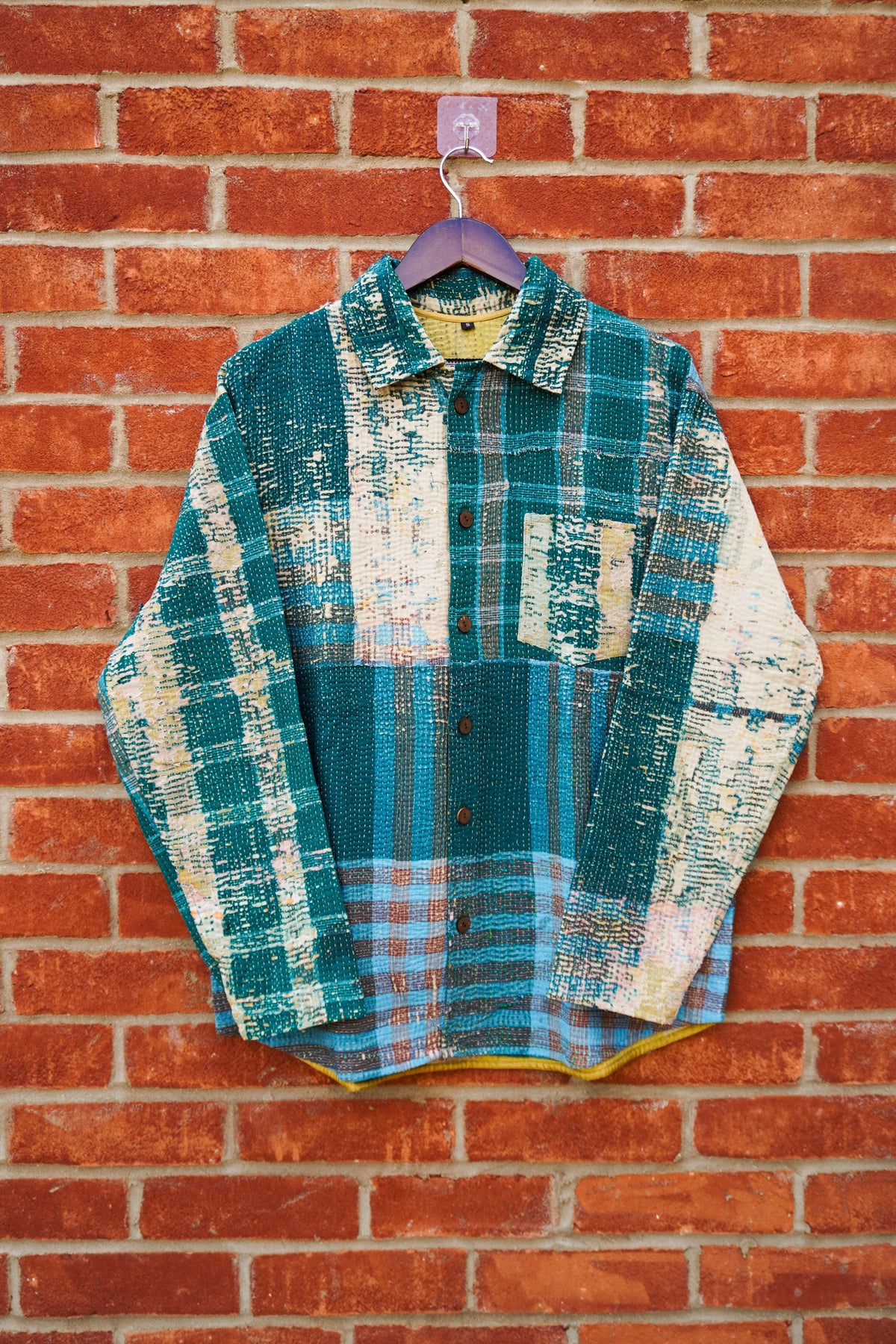 A model viewed from behind wearing a long-sleeve button-up vintage kantha shirt with a colorful, painterly horizontal stripe pattern in orange, blue, pink, and gray, paired with black jeans against a warm off-white background.