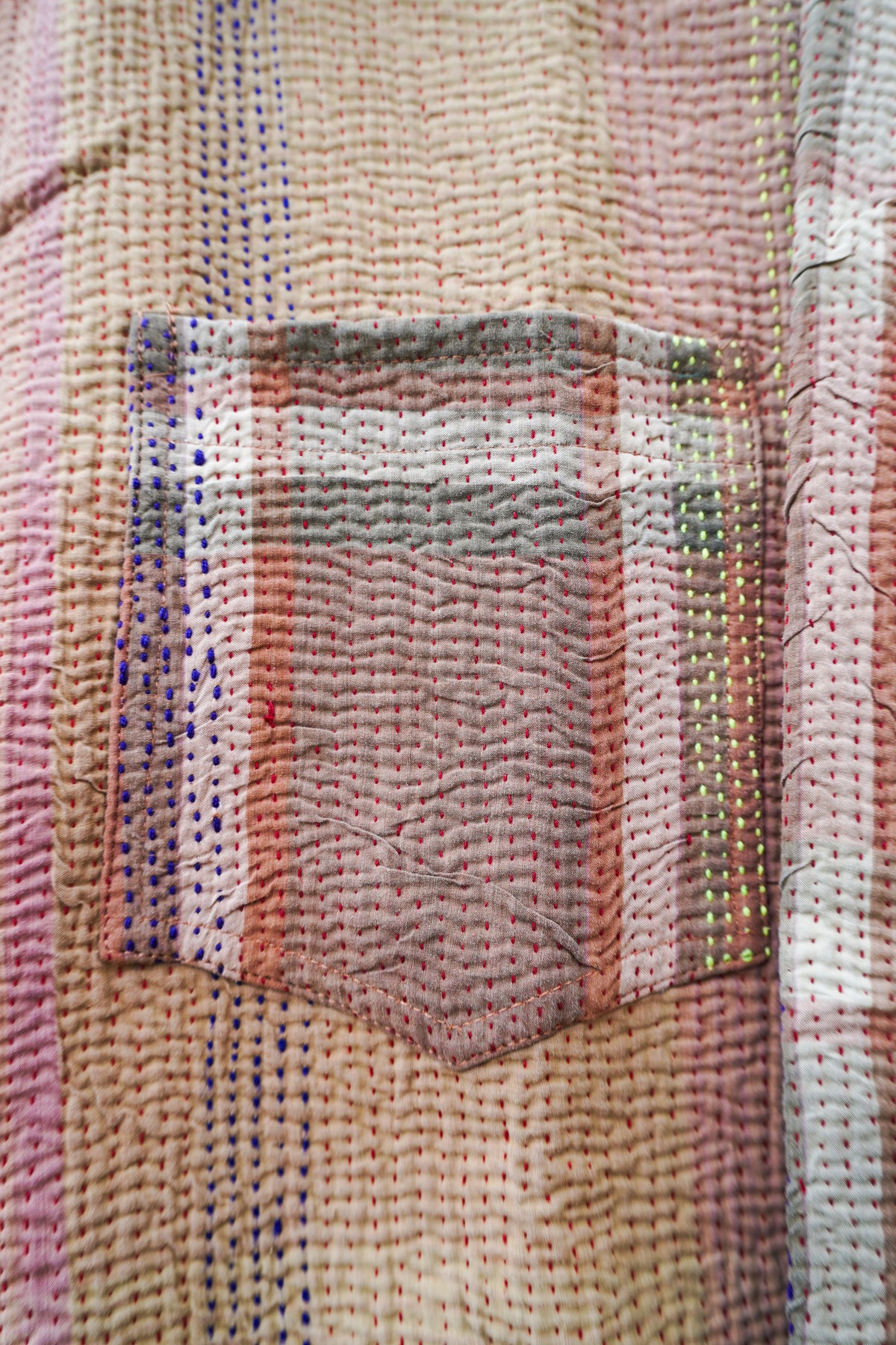 Close-up of a textured, hand-woven fabric pocket with a multicolor plaid pattern in pink, beige, orange, and blue threads.