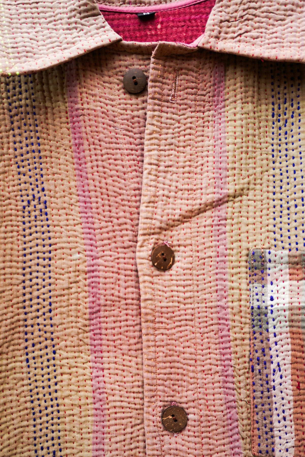 Close-up of a textured woven jacket with a collar, brown buttons, and vertical stripes in pink, beige, and blue.