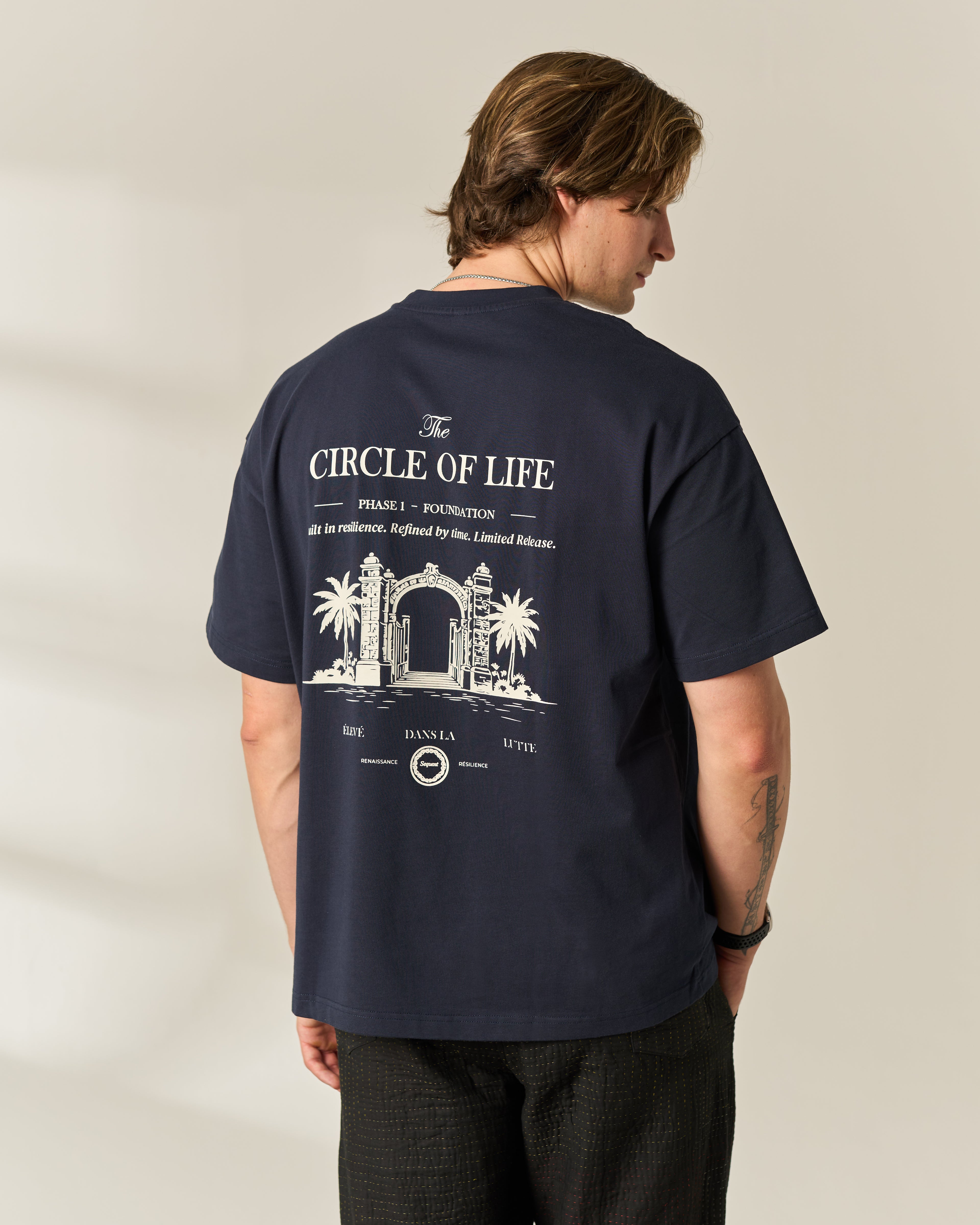 A man wearing a navy blue t-shirt from the back, featuring a large white graphic print with the text 'CIRCLE OF LIFE'.