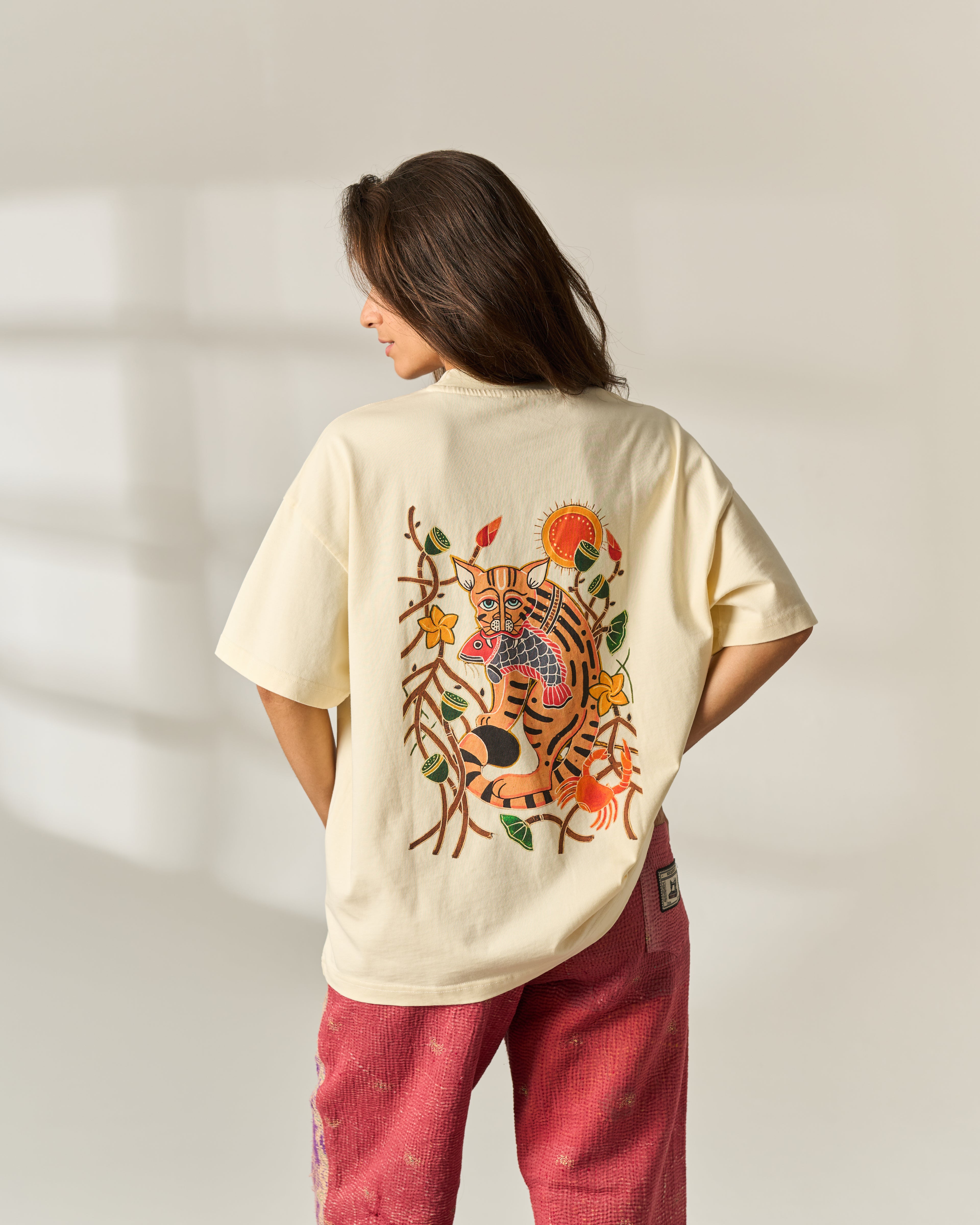 A woman viewed from behind wearing an oversized cream-colored t-shirt with a large, colorful embroidered tiger and floral design on the back, paired with pink pants.