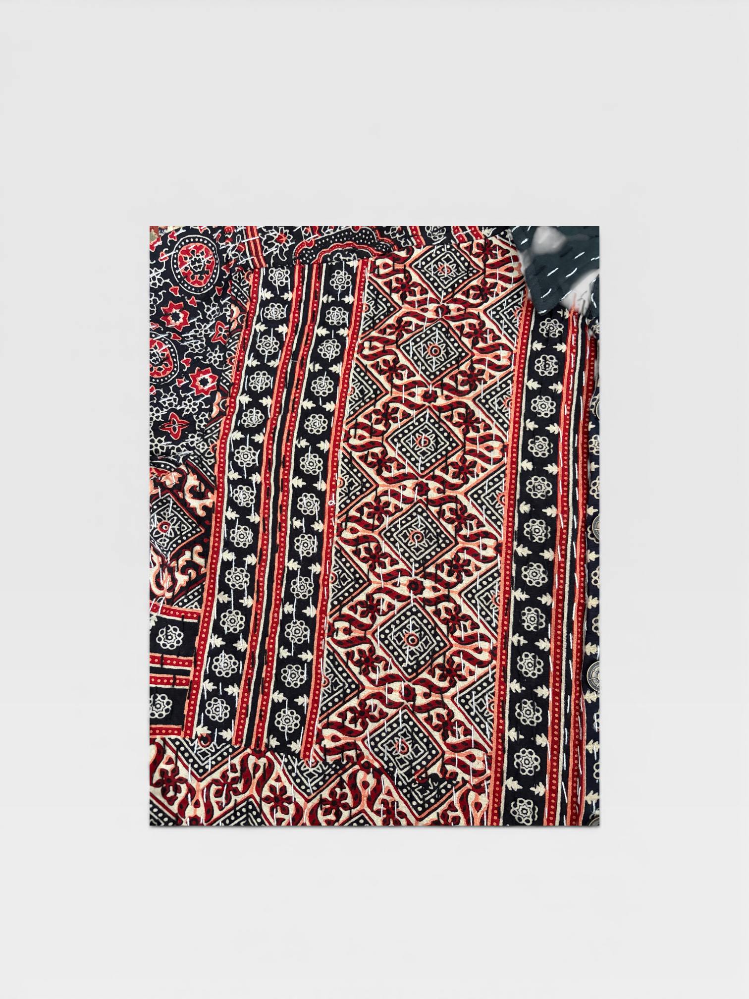 Traditional Ajrakh Kantha fabric with red, black, and white colors on a light gray background