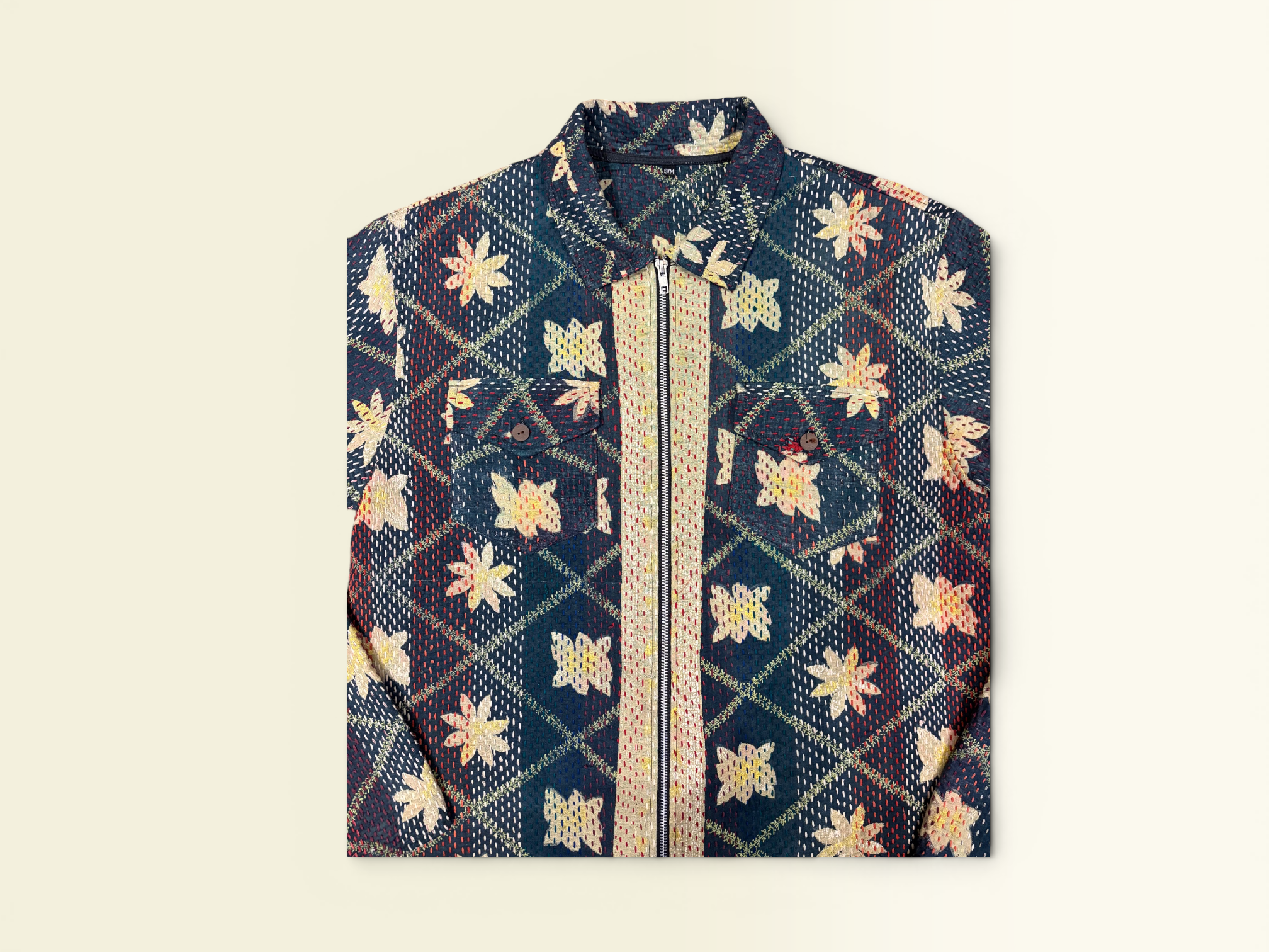 A folded long-sleeve button-up Vintage Kantha jacket with a navy blue base and a detailed batik-style pattern in beige, gold, and red, featuring a central vertical gold stripe.