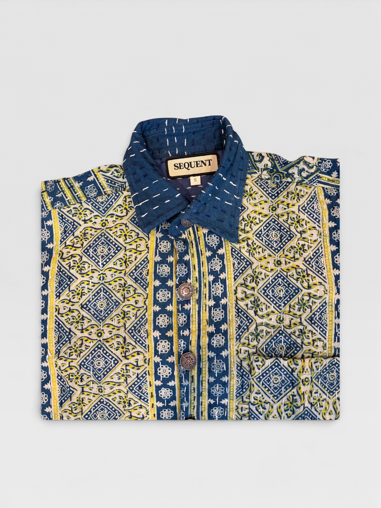 Blue and yellow patterned Ajrakh Kantha shirt with 'Sequent' label on a light gray background